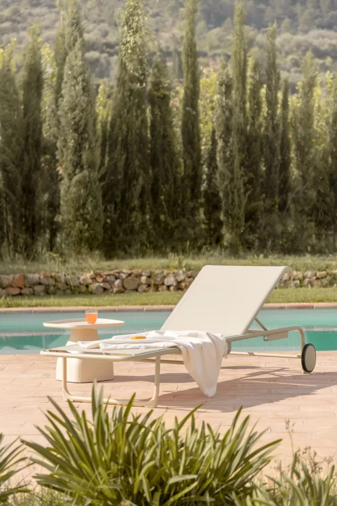 Tumbona reclinable de aluminio con mesa auxiliar junto a una piscina en un entorno natural, ideal para la decoración de piscinas modernas.