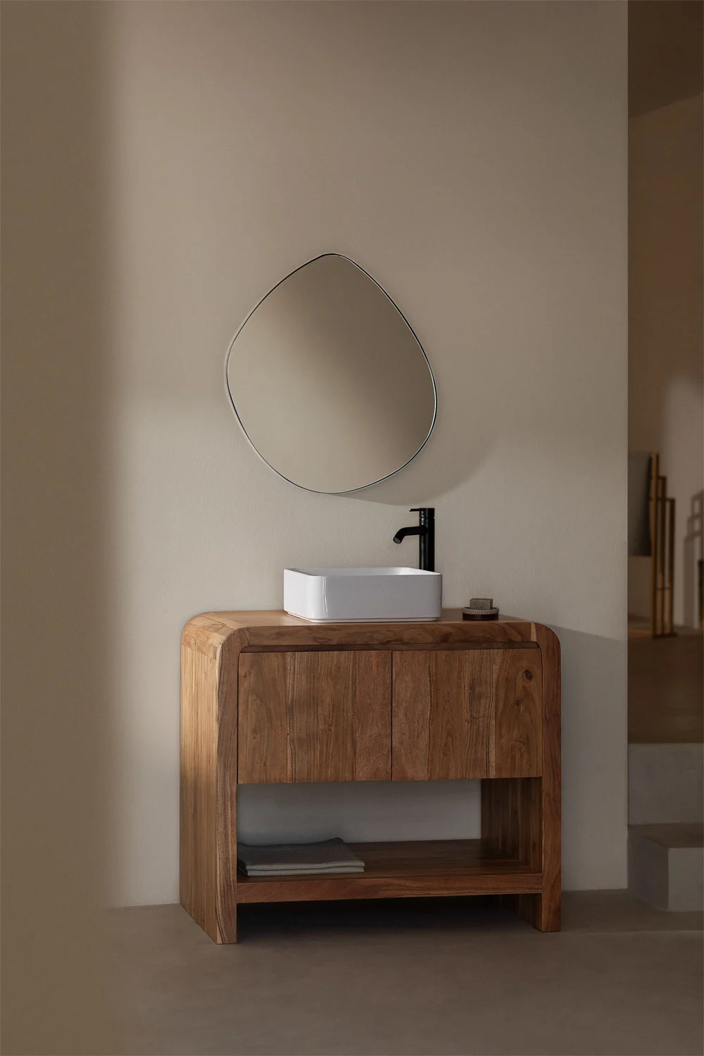 Baño con mueble de madera maciza y lavabo sobre encimera, acompañado de un espejo orgánico y grifería negra, combinando diseño rústico y contemporáneo.