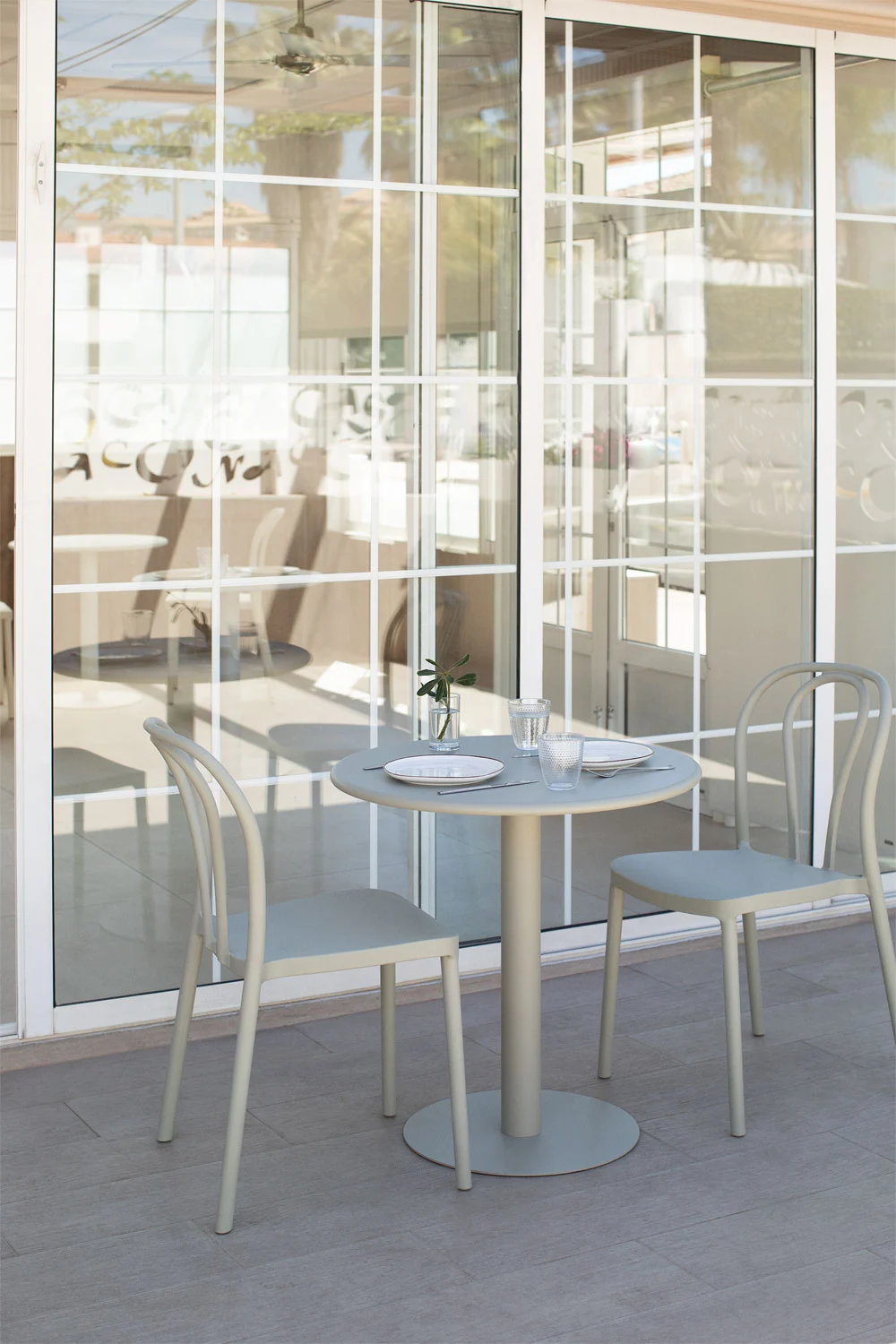 Pequeno terraço com mesa redonda e cadeiras de metal cinza, criando um espaço exterior moderno e funcional.